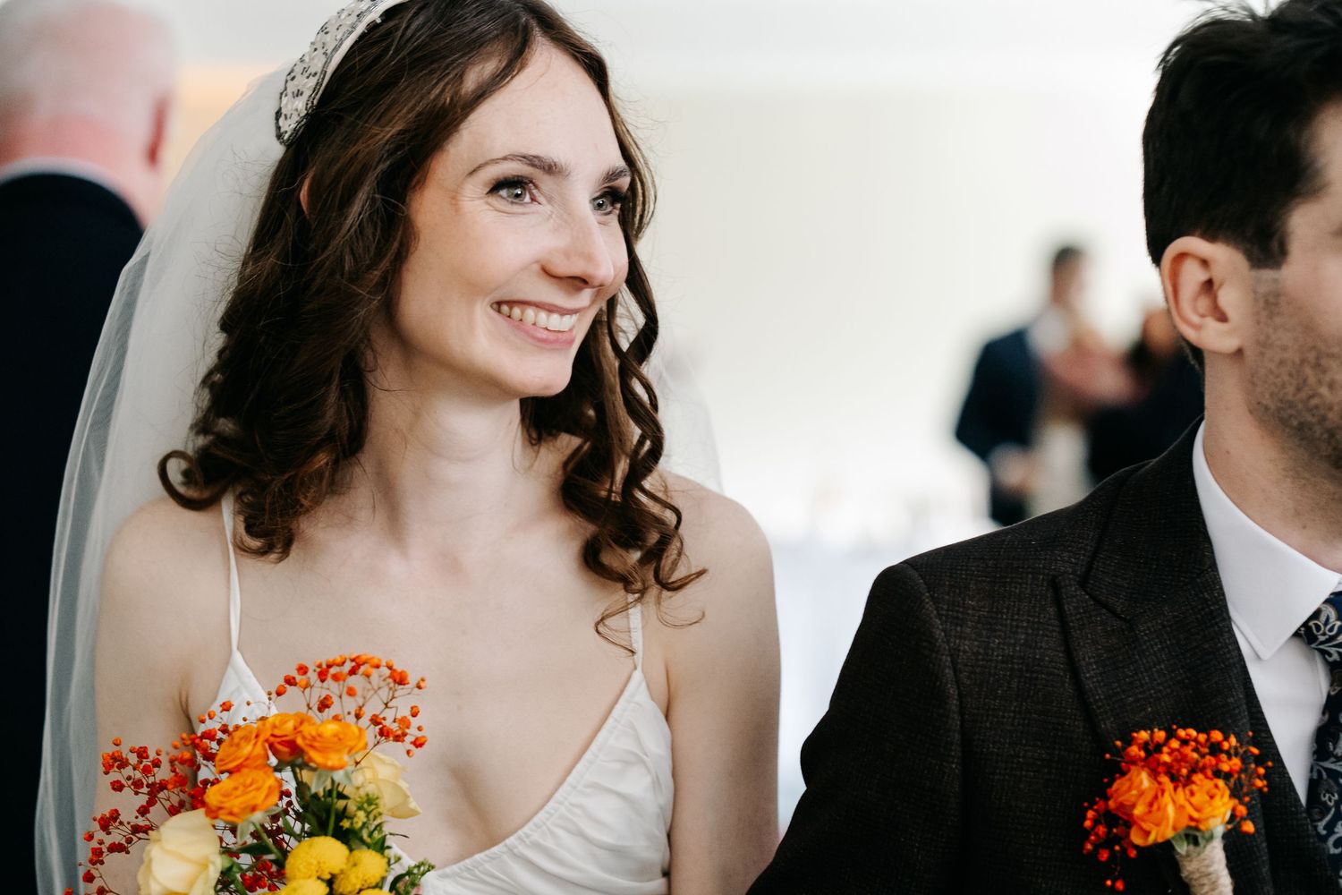 A bride in white holds a vibrant orange and yellow bouquet during her wedding day.