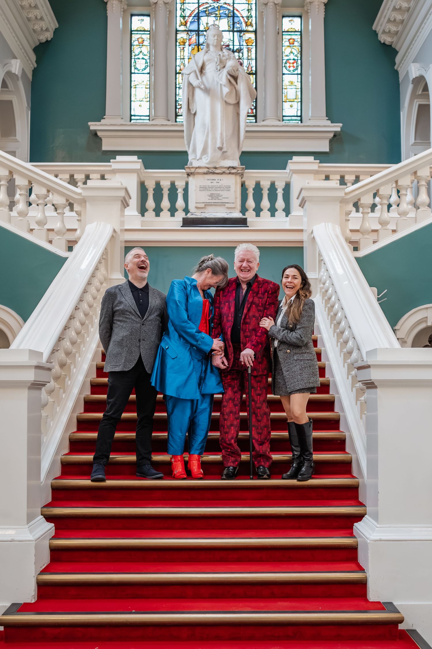 Grand staircase with red carpet and white balustrade in historic building interior.