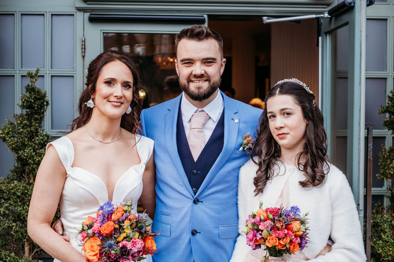 Wedding party stands together outside venue wearing coordinated blue and white attire.