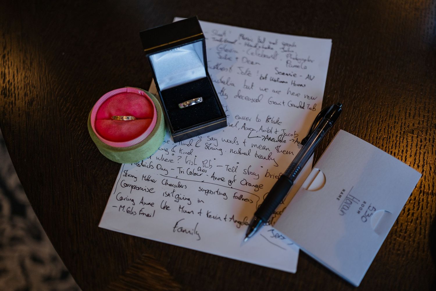 Handwritten love letter with engagement ring in box, gold band, pen, and envelope on dark wood table.