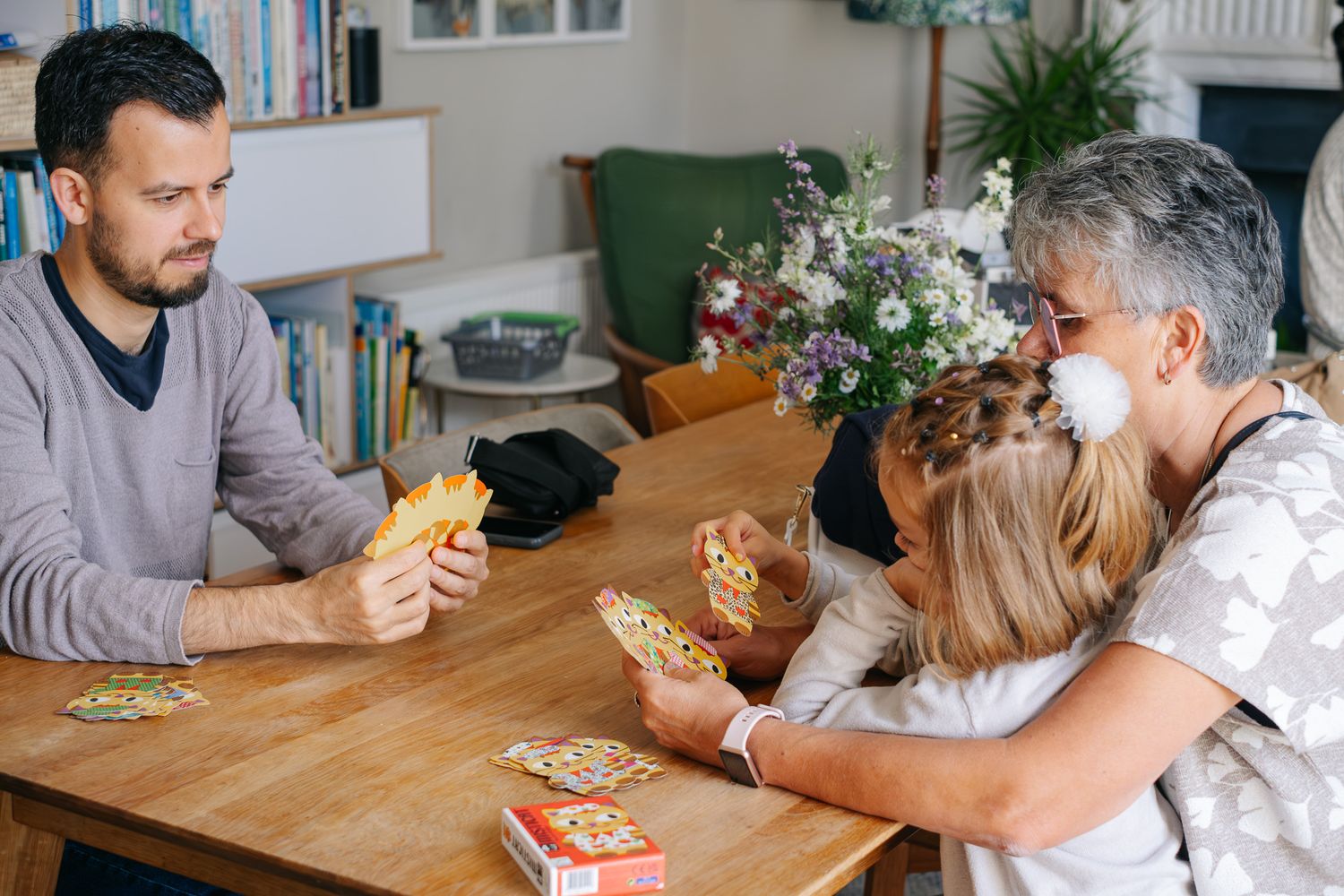 Family playing a card game together at a wooden dining table in a cozy home setting.
