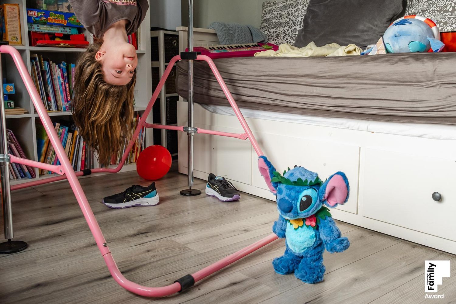 A pink vacuum cleaner and blue toy move across a hardwood floor while cleaning under furniture.