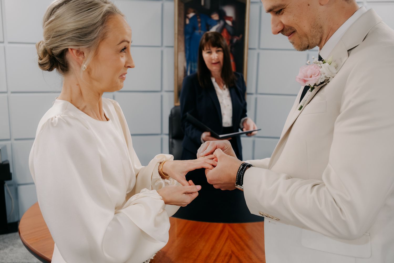 Bride and groom exchanging rings during intimate wedding ceremony with officiant in background.