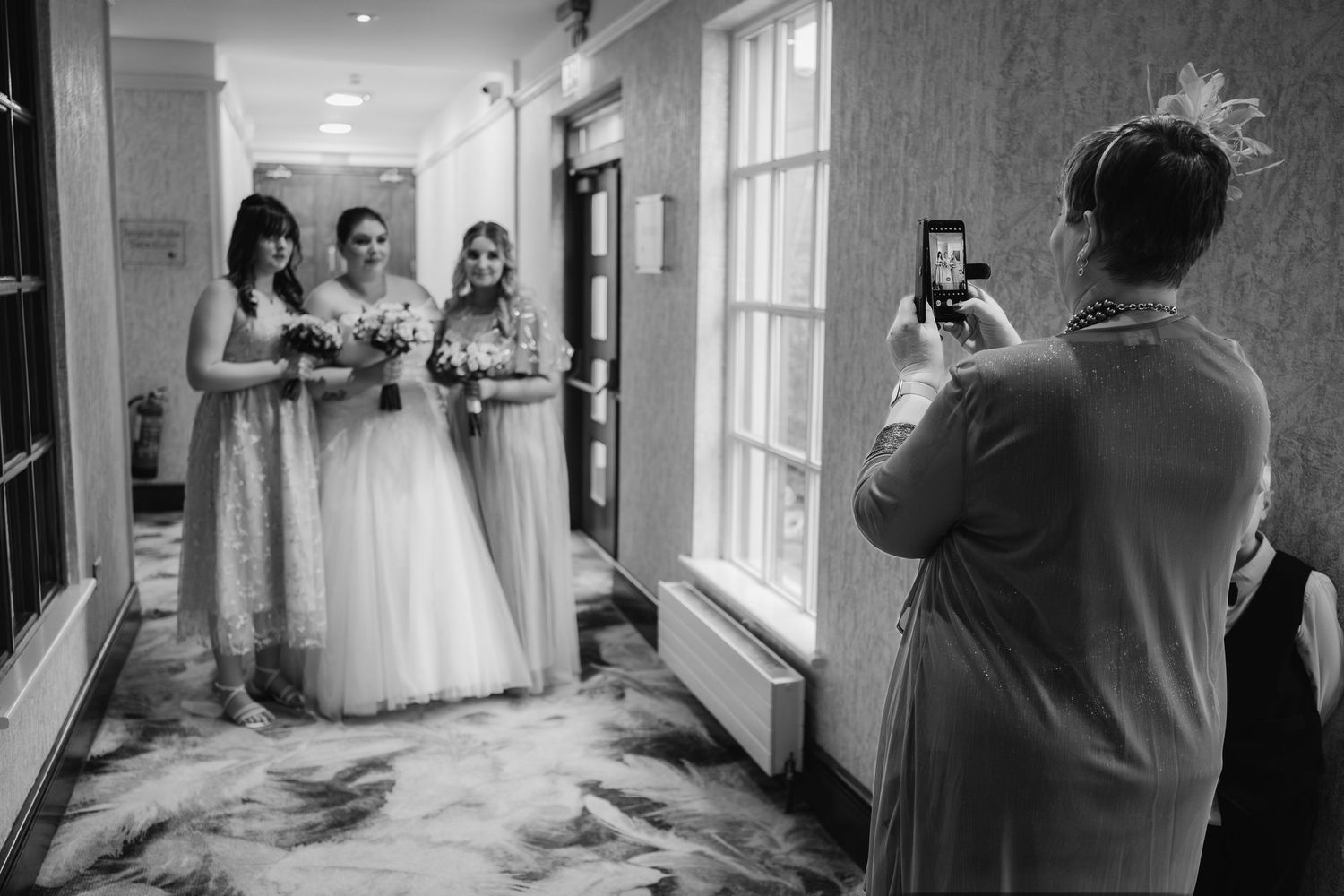 Black and white photo of wedding party being photographed in elegant hallway.
