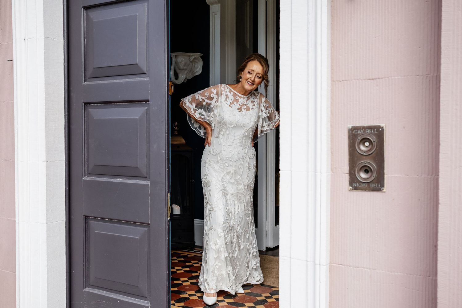 A person in a white lace wedding gown poses in an elegant doorway.