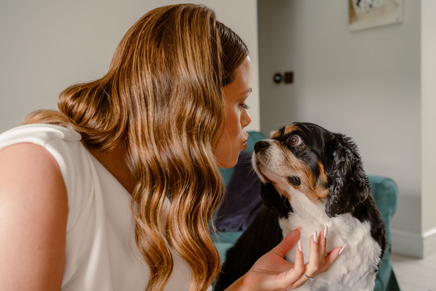 Woman in white dress bending down to kiss Cavalier King Charles Spaniel dog.