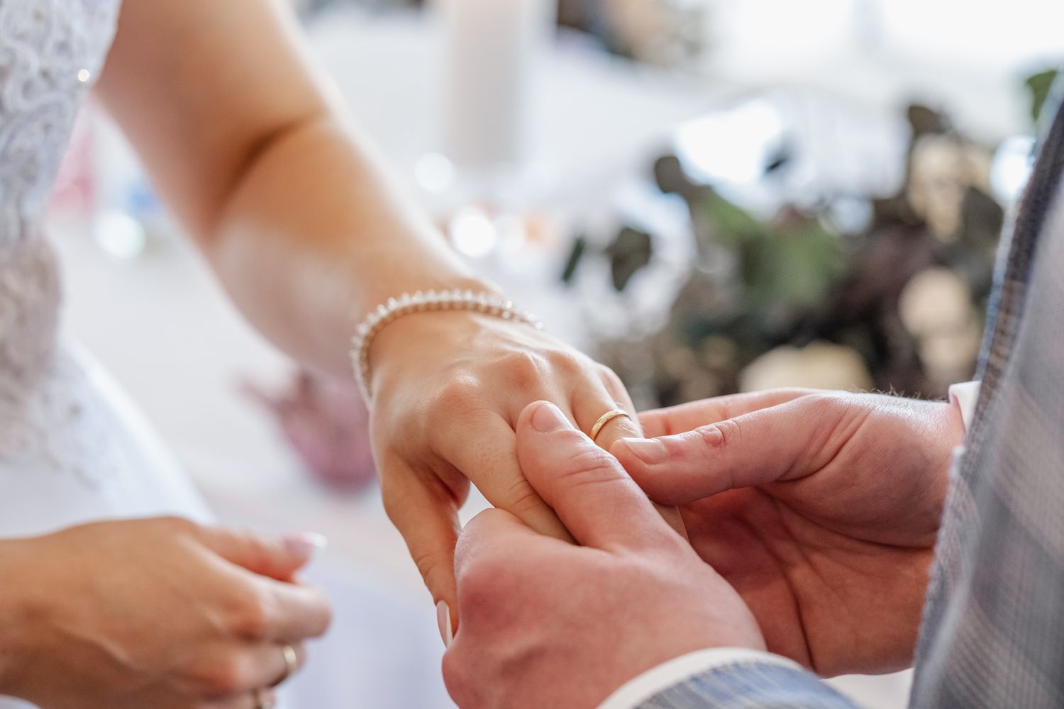 Groom placing a wedding ring on bride's finger during ceremony, bride wearing pearl bracelet.