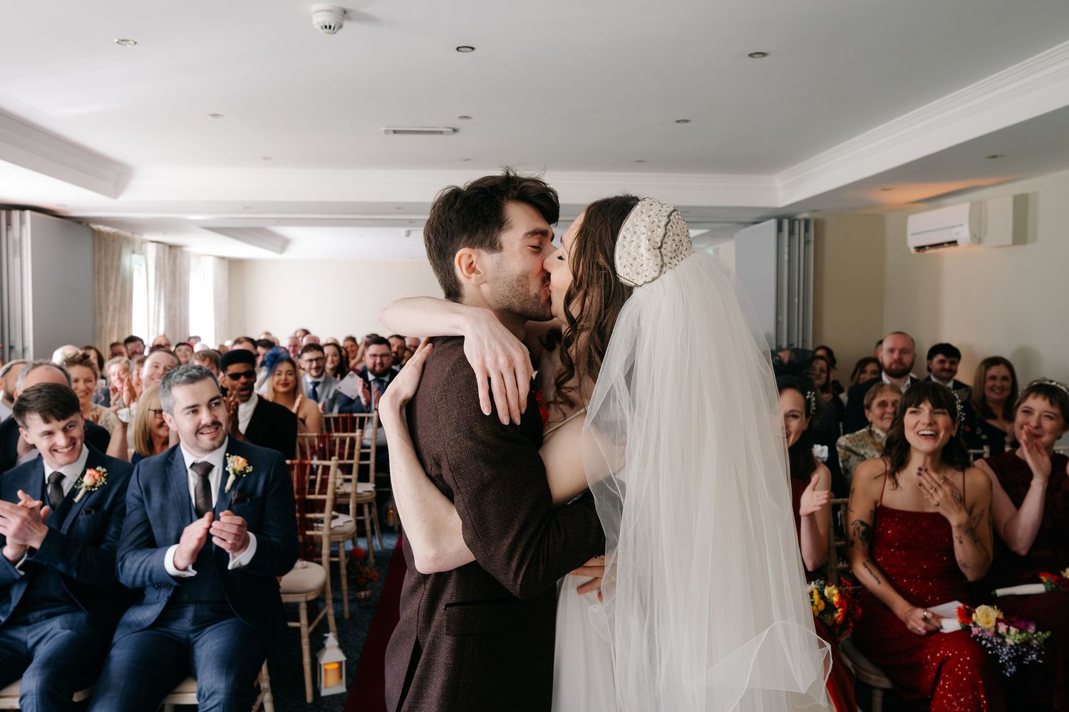 Wedding ceremony guests stand and celebrate in an elegant white room.