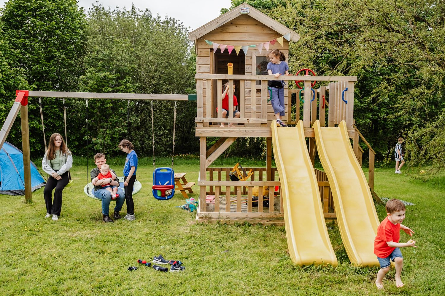 Children playing on wooden playground structure with slide in backyard setting.