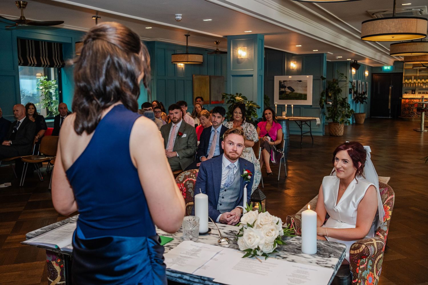 Wedding reception guests seated at decorated tables in a modern venue with teal accents.