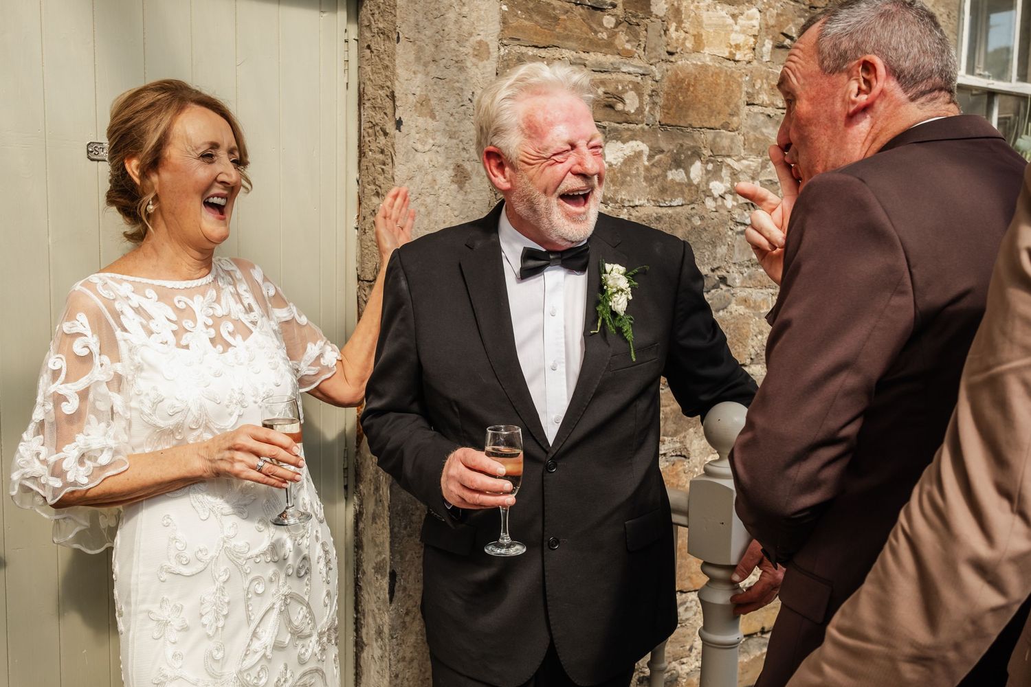 Wedding guests sharing laughter and drinks at an elegant stone venue.