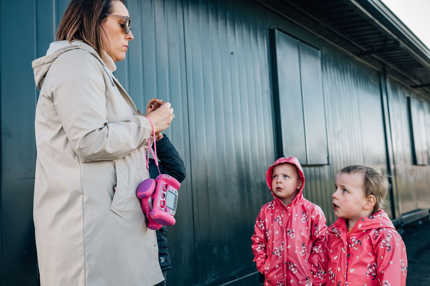 Children in matching pink raincoats having a conversation outdoors.