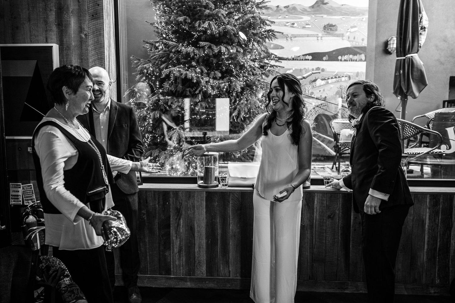 Black and white photo of bride in white dress at wedding reception bar with guests.