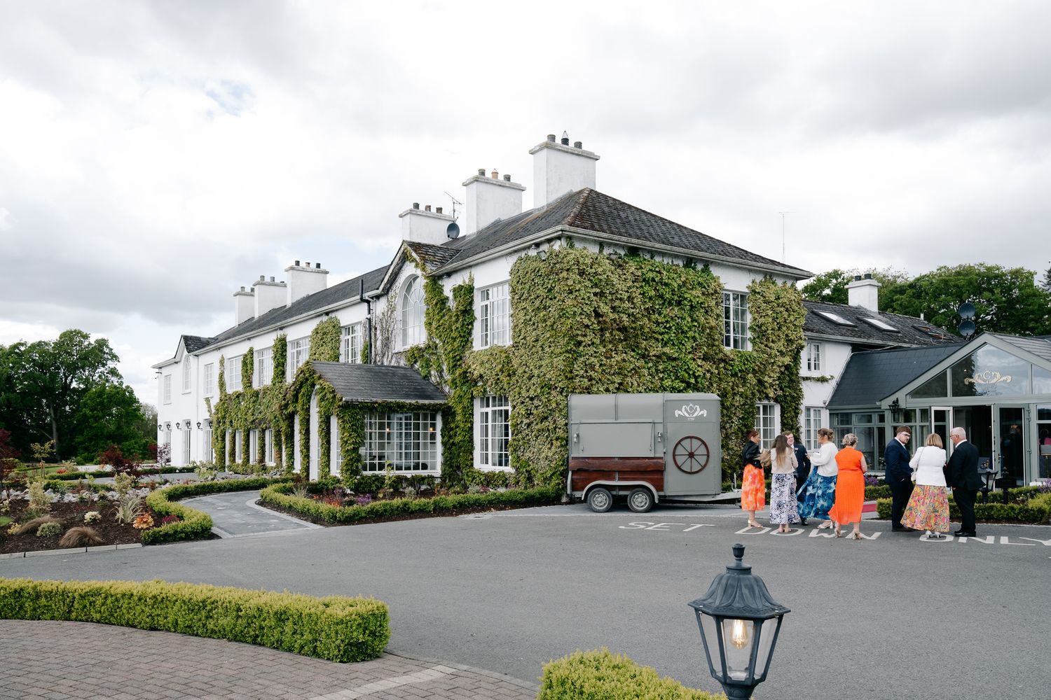 Ivy-covered white manor house wedding venue with horse trailer and guests arriving on a cloudy day.