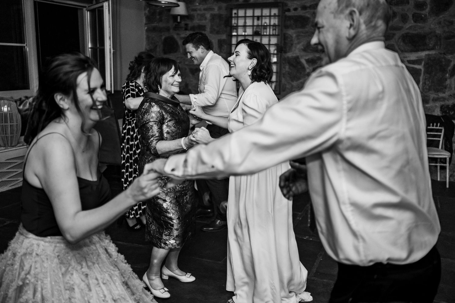 Black and white photo of guests holding hands and dancing together at a wedding.