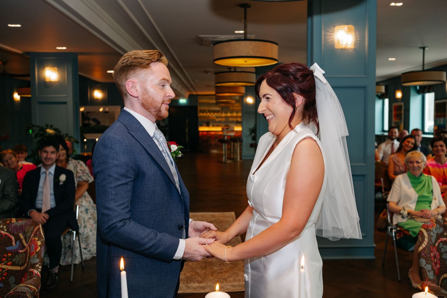 Wedding couple holding hands during their ceremony in a modern venue with teal walls.