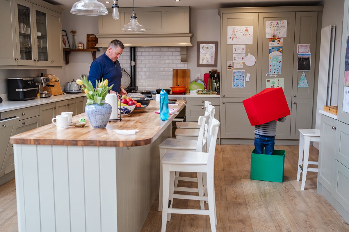 Modern kitchen with dad prepping food and child standing in a box with another box in his head.