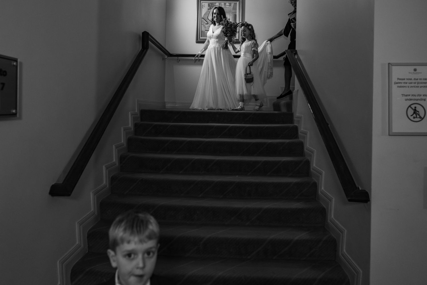 Black and white wedding photo of bride on stairs with surprised boy in foreground.