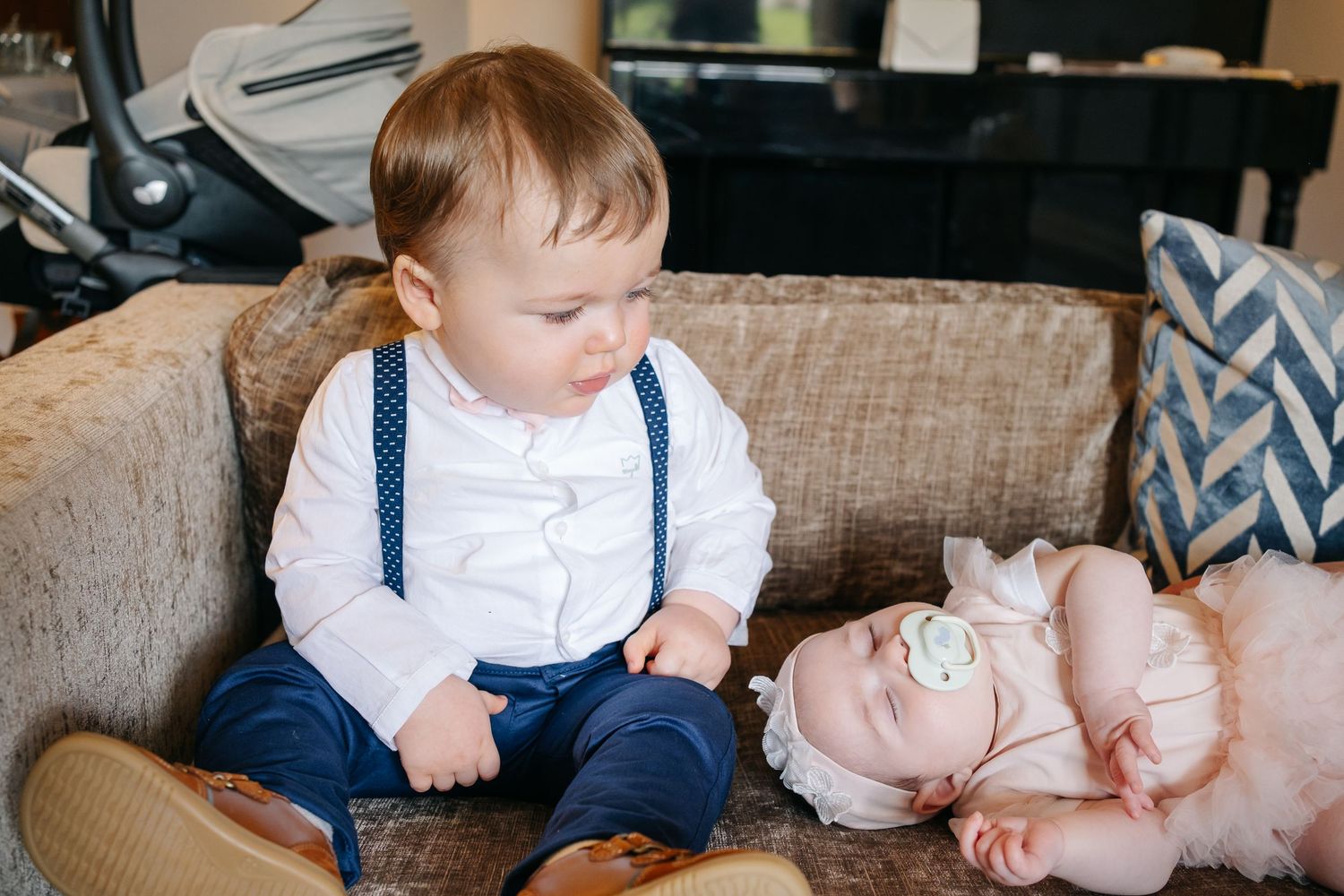 Toddlers in coordinated navy and white outfits playing on beige couch with decorative pillows.