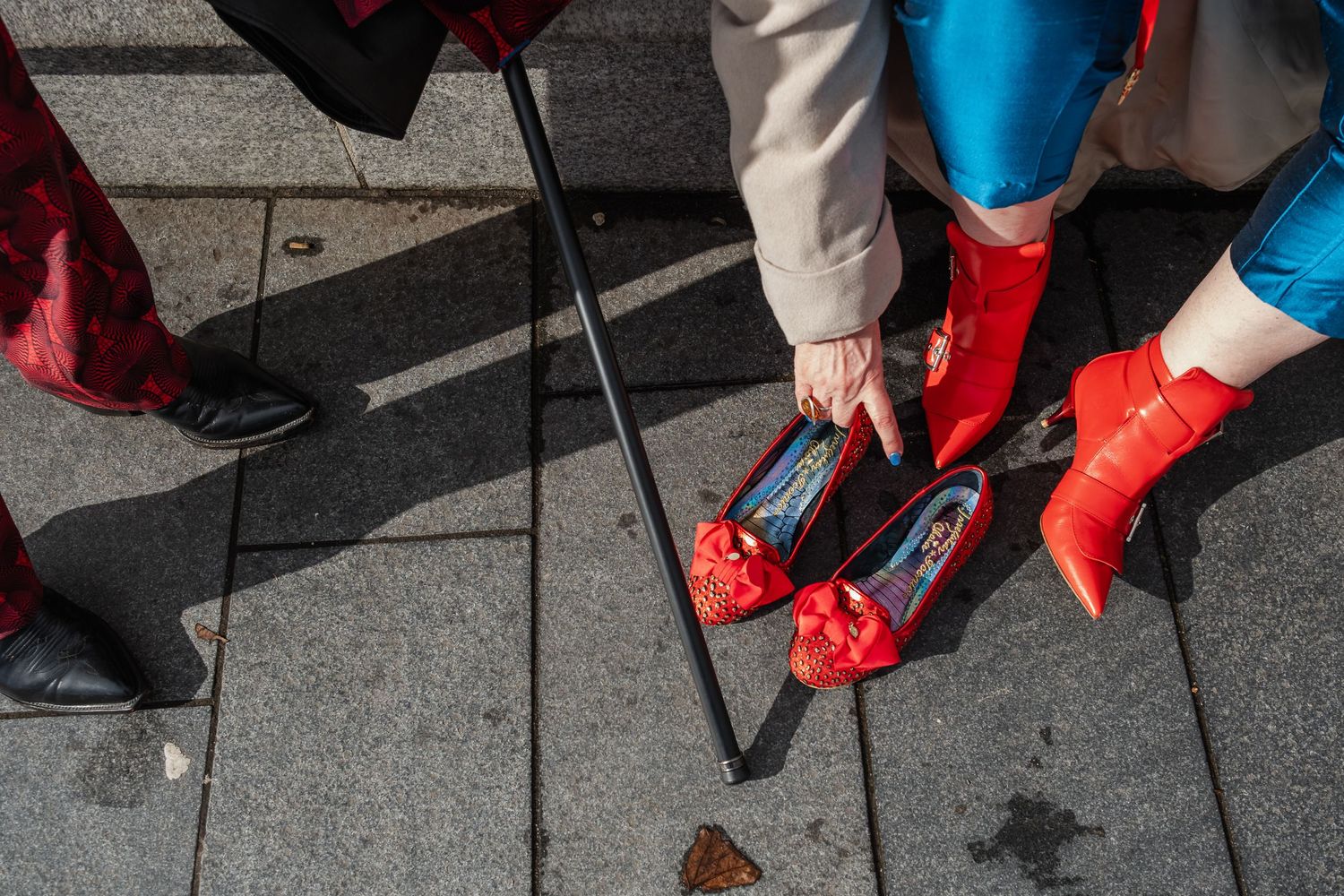 Close-up of bright red shoes and a walking cane on gray paved ground.