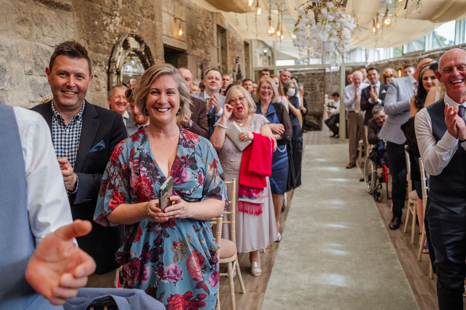 Wedding guests lined up in aisle clapping and celebrating during wedding ceremony.
