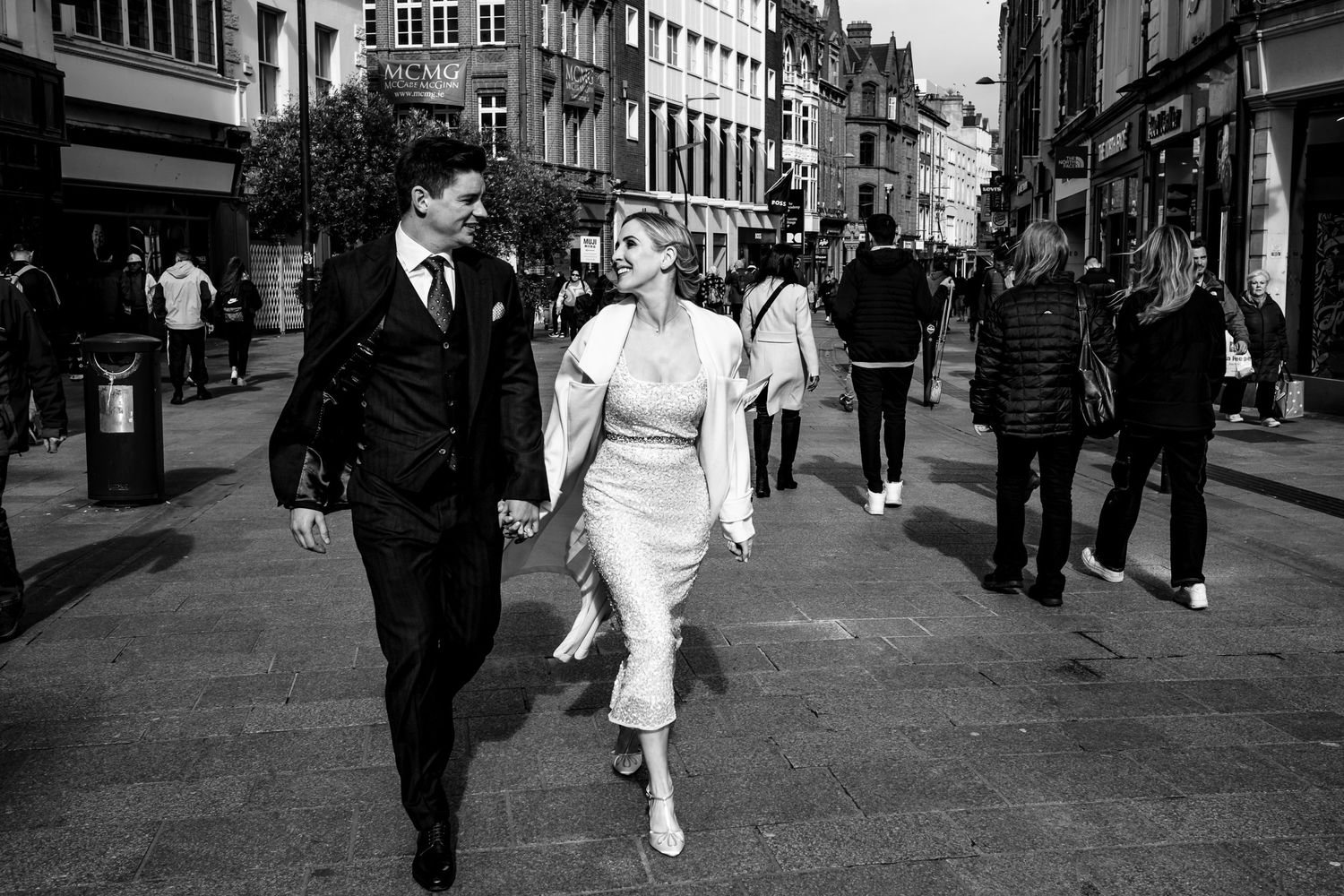 Couple in vintage-style attire strolling down a busy city street in black and white.