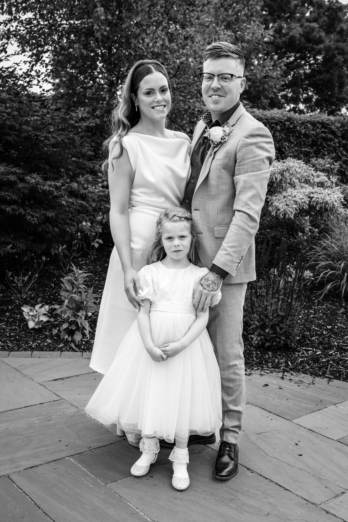 Black and white wedding portrait on stone paving surrounded by garden landscaping.