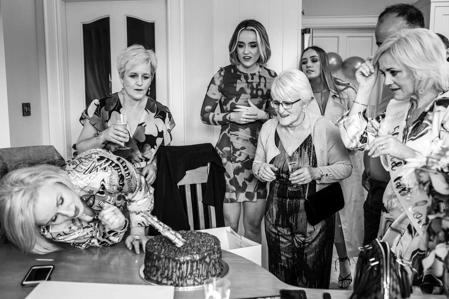 A black and white image of adults examining a birthday cake at a 50th birthday party.