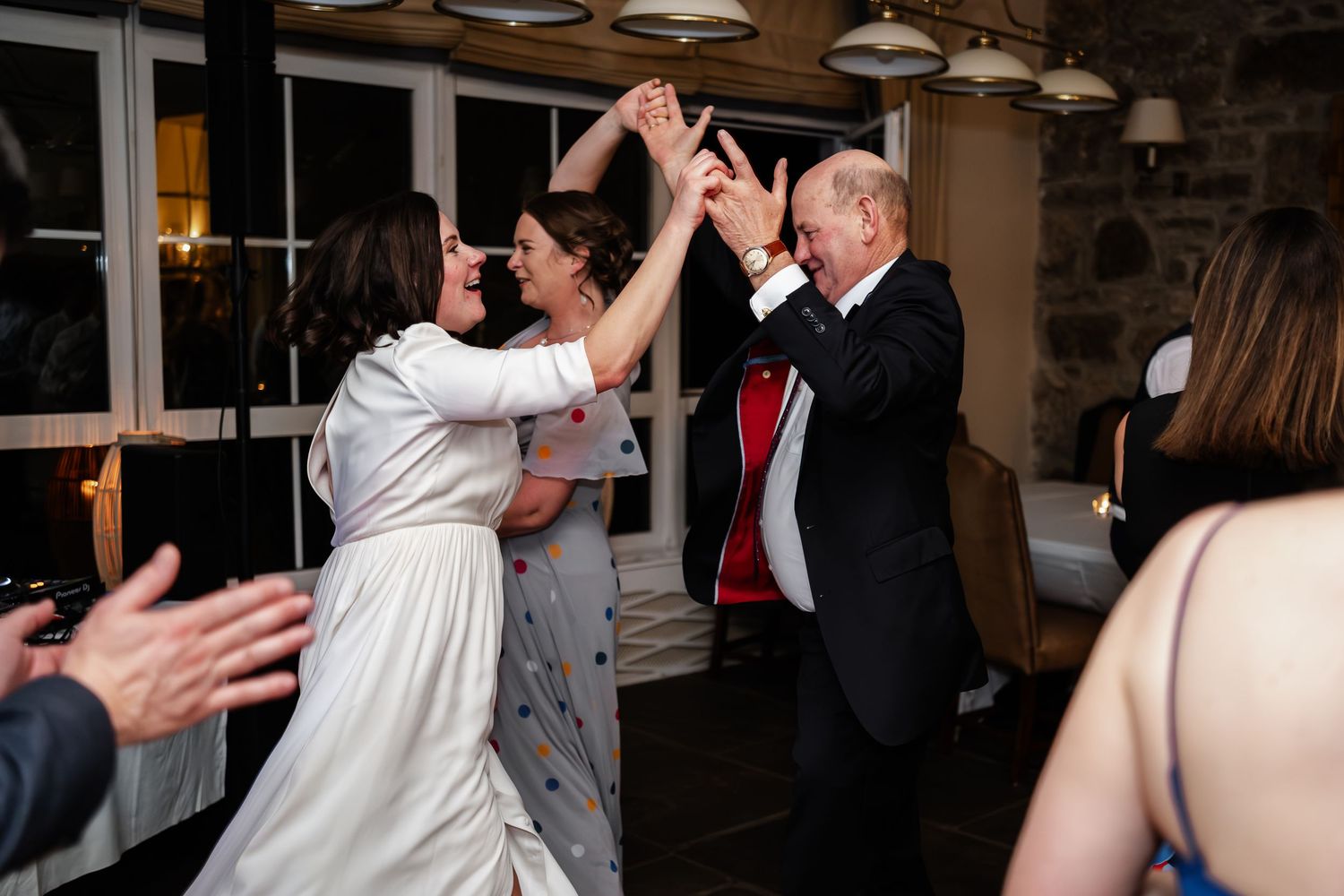 Bride and older man dancing joyfully at a wedding reception in a rustic venue.