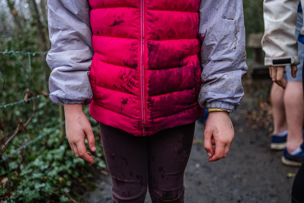 Child wearing a pink puffer vest and purple pants standing on an outdoor path surrounded by greenery.