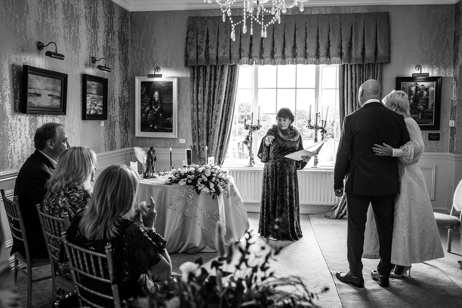 Intimate wedding ceremony with couple embracing before officiant in elegant room.