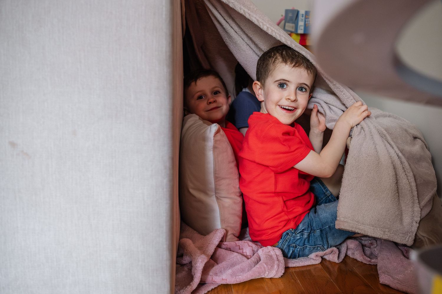 Children playing and hiding under blankets in a cozy home setting.
