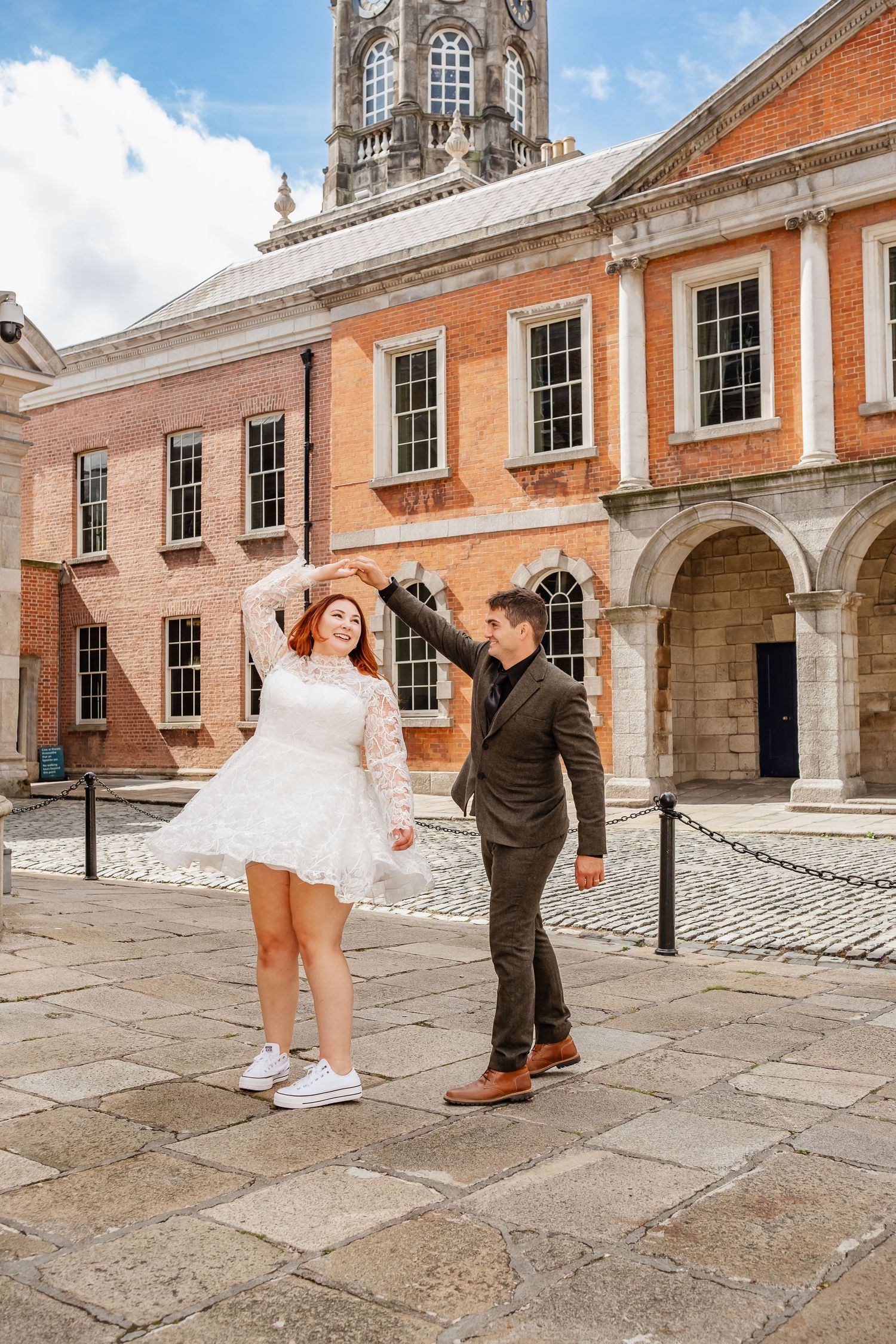 A couple dancing joyfully outside a historic Georgian building with classical architecture and a clock tower.