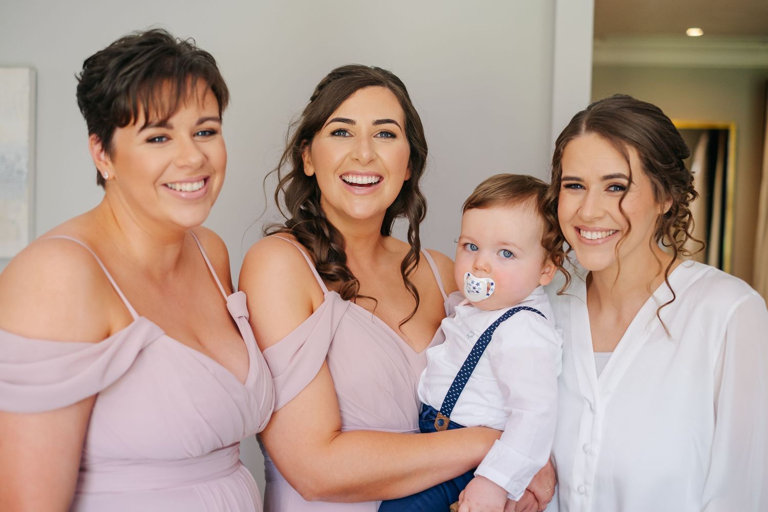 Wedding party in pale pink and white attire gathered together for pre-ceremony photos.