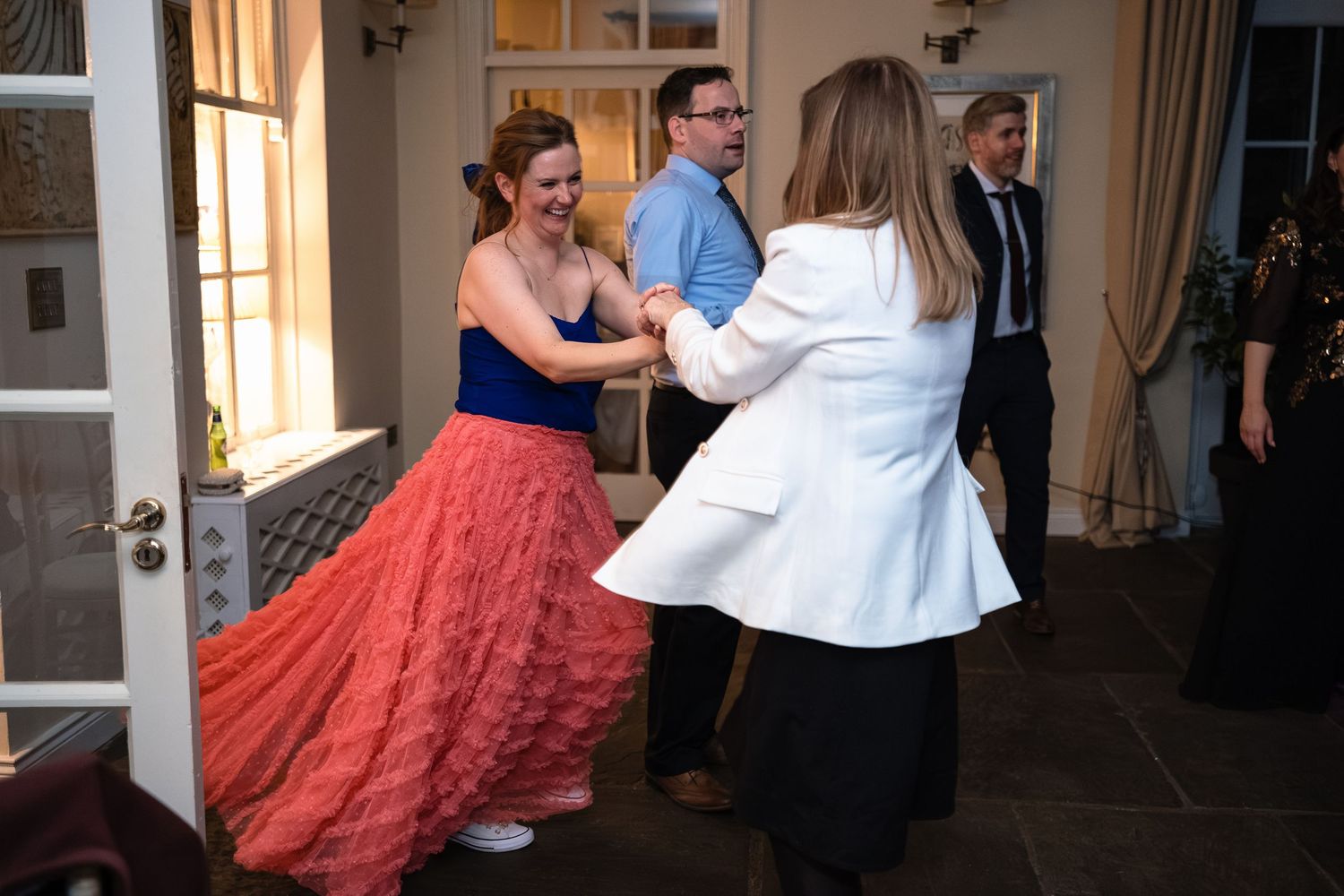 Woman in red ballgown dancing with guests at elegant indoor formal event.