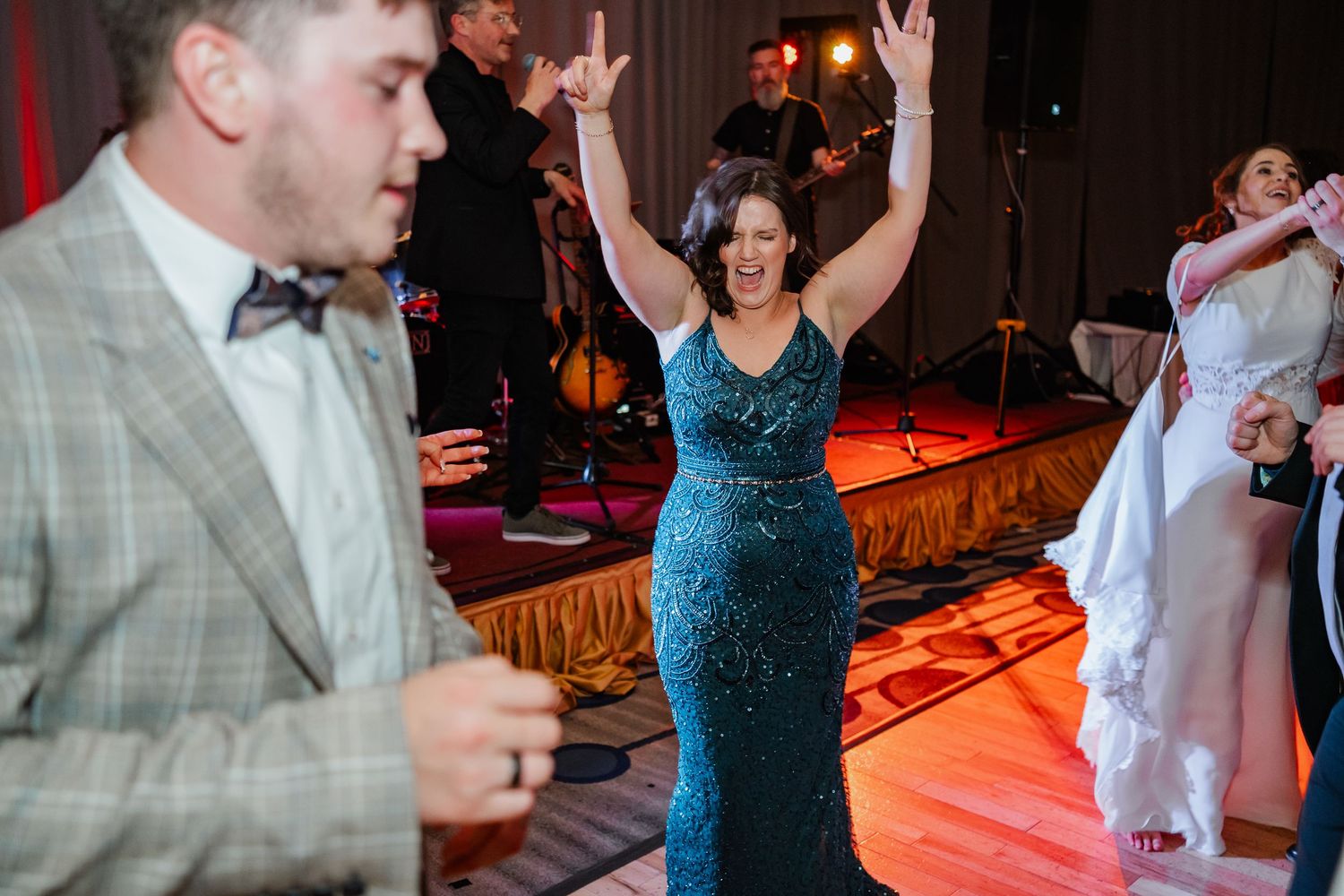 People dancing and celebrating at a wedding reception with red ambient lighting and a glowing dance floor.