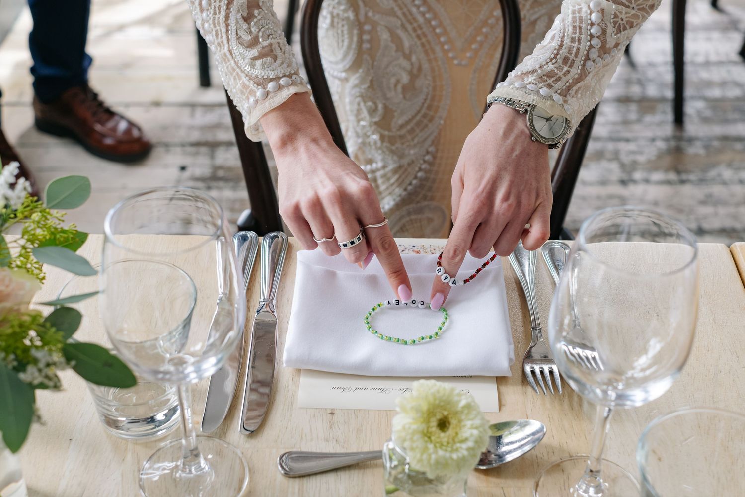 Hands are seen plating and serving food at an elegant white tablecloth dining event with crystal glassware.