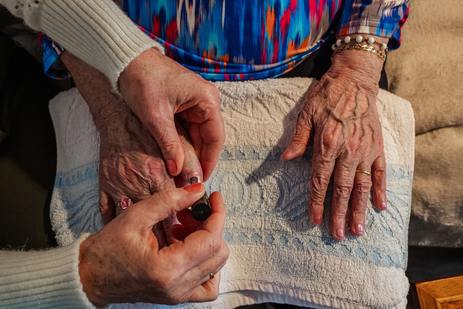 Elderly hands with wrinkles and jewelry resting on white fabric.
