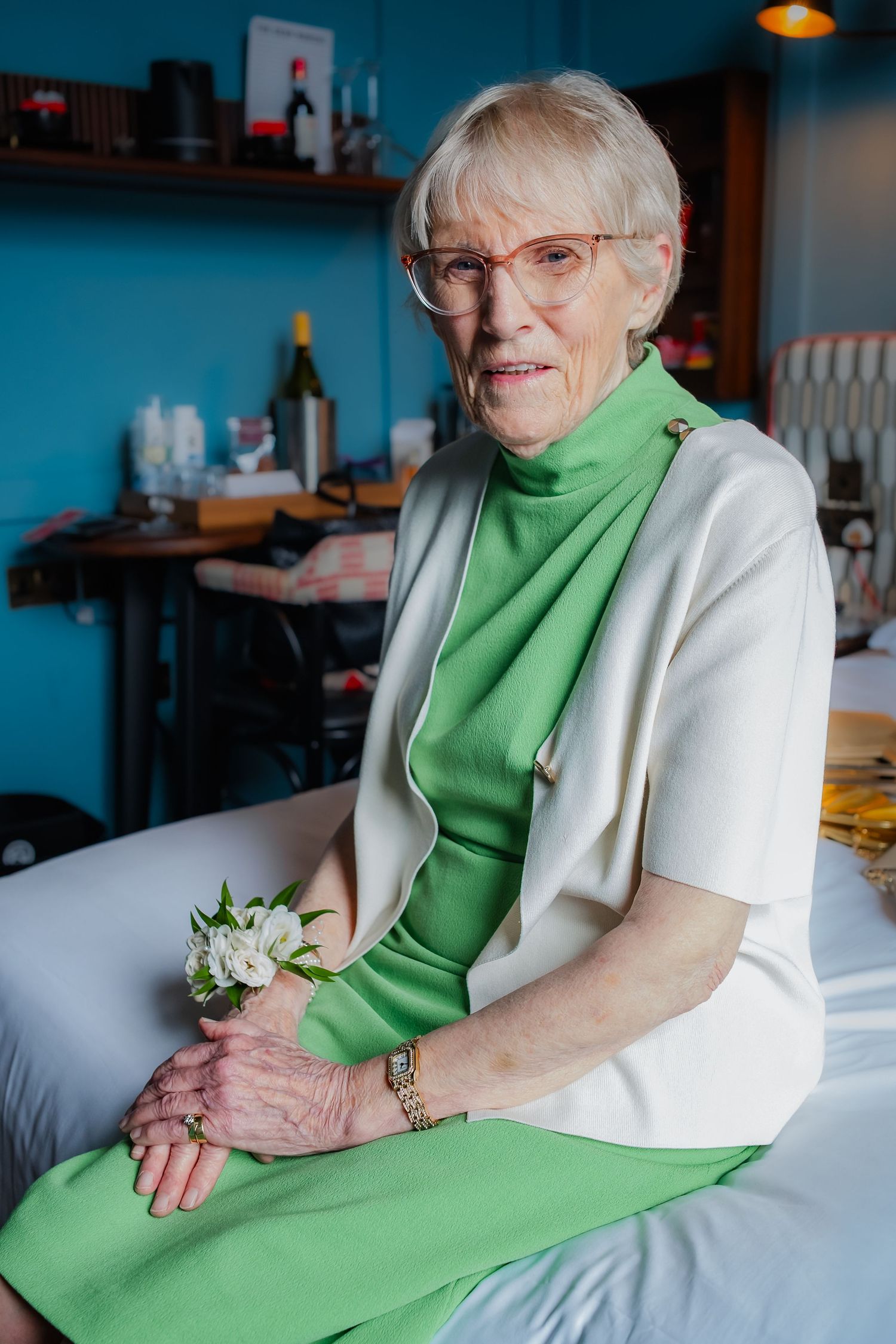 An elegant guest wearing a green dress and white jacket seated in a modern blue-walled venue.