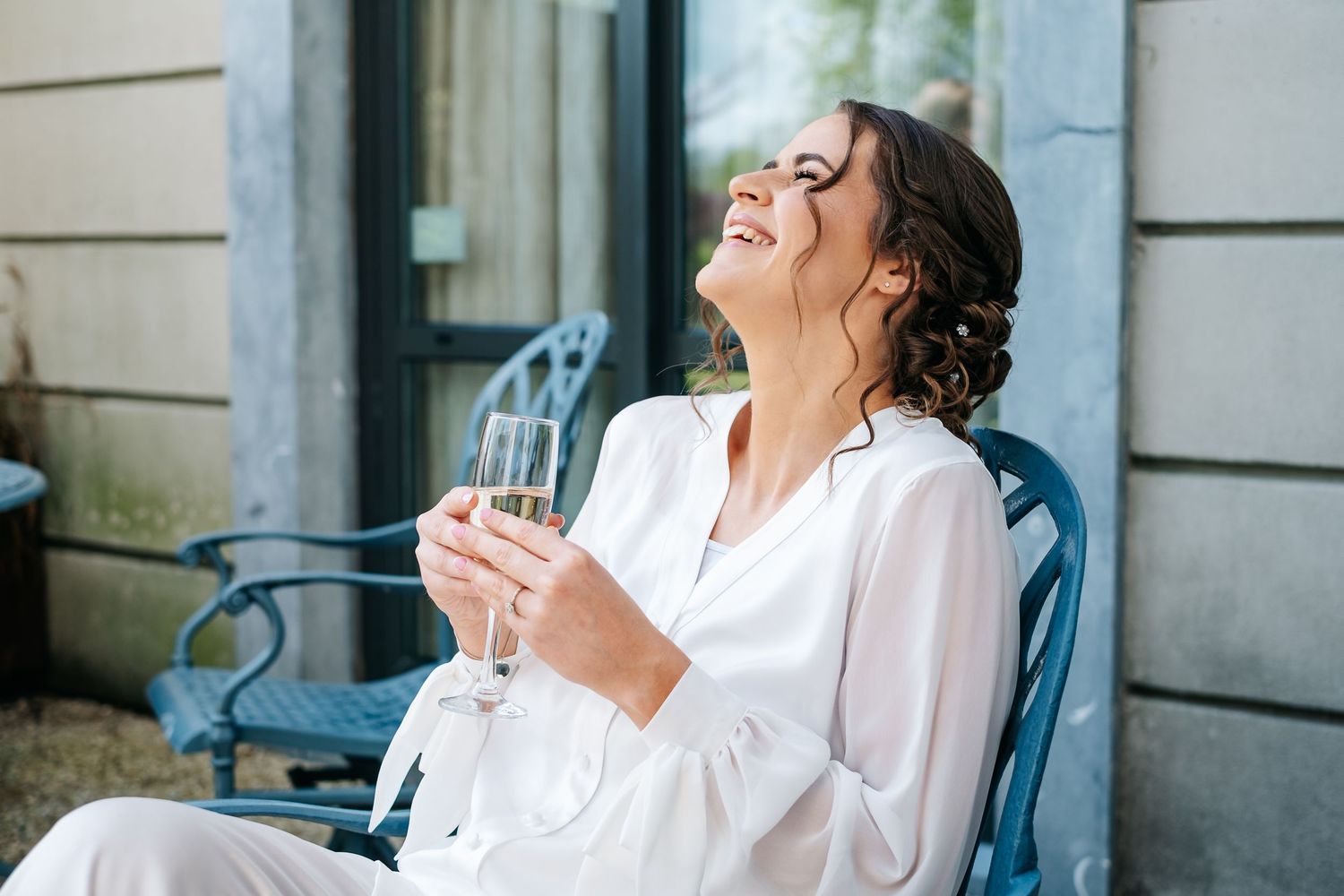Woman in white blouse sitting at outdoor cafe table laughing joyfully during a sunny afternoon.