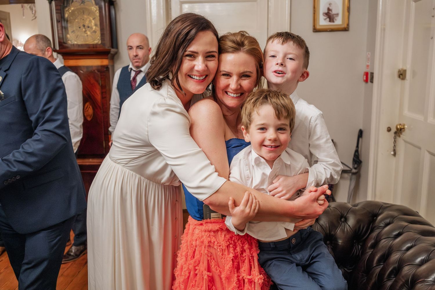 Two women and two young boys share a joyful group hug at a wedding celebration.