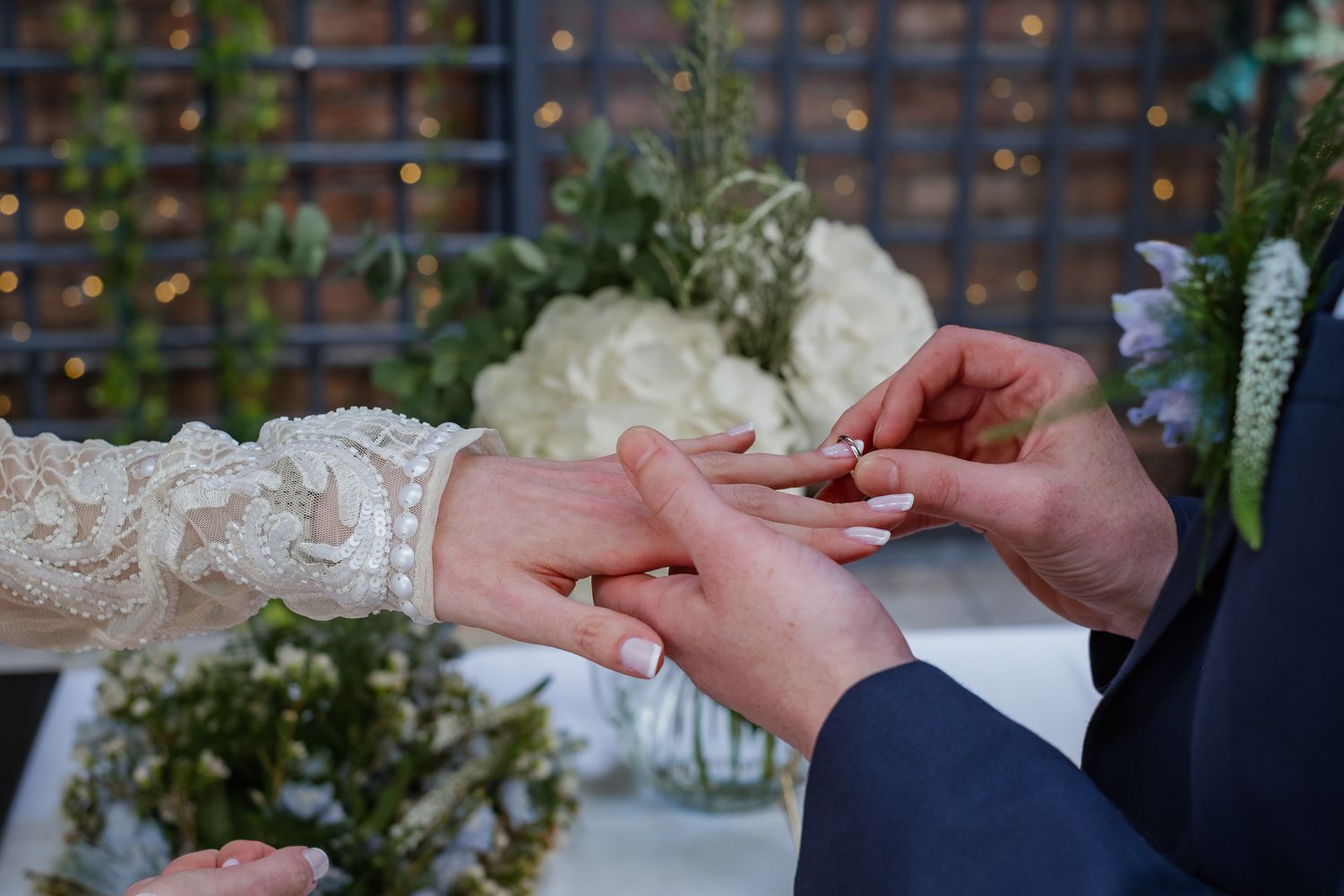 Close-up of hands exchanging rings during wedding ceremony with floral backdrop.