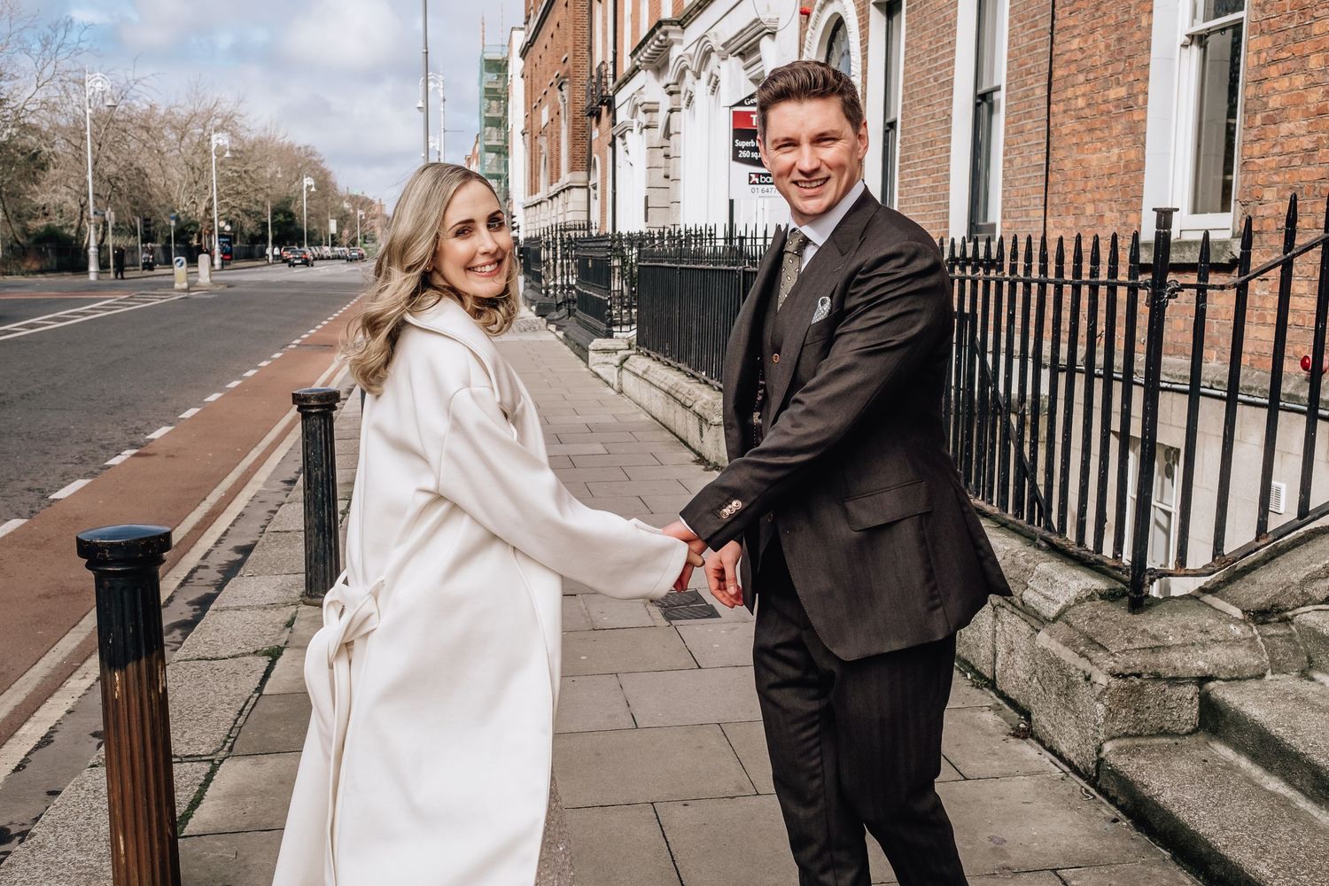 Couple walking together on a charming brick-lined street in formal attire.