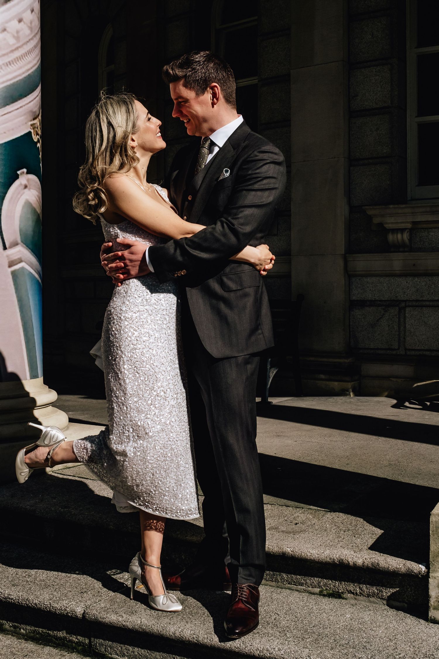 A romantic couple embraces on stone steps, with the bride wearing a sparkly dress.