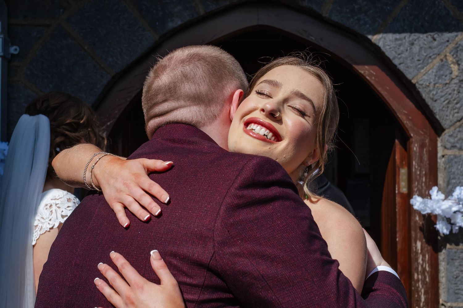 Wedding embraces and hugs shared between guests in burgundy formal wear.