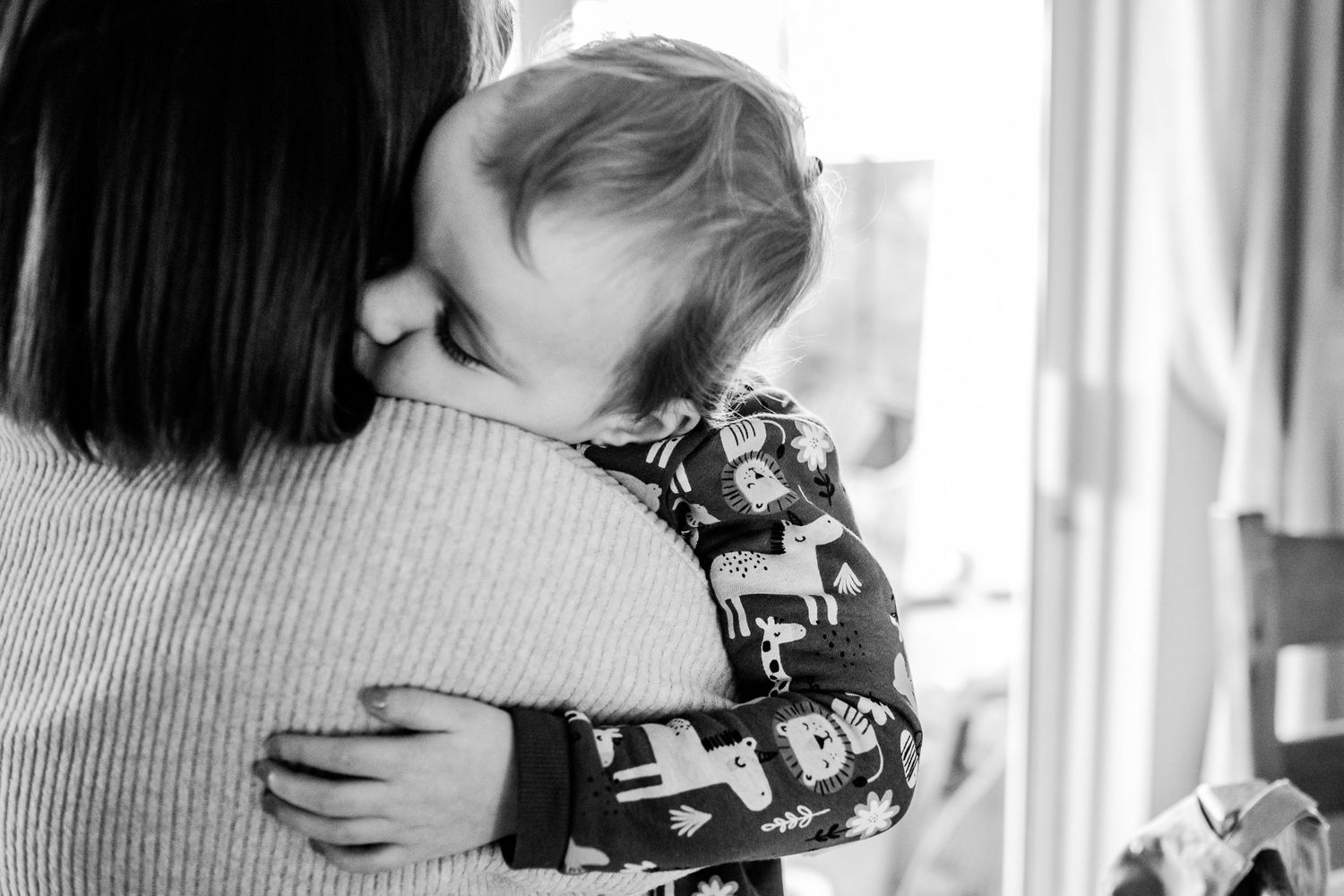 Black and white intimate moment showing embrace against soft window light.