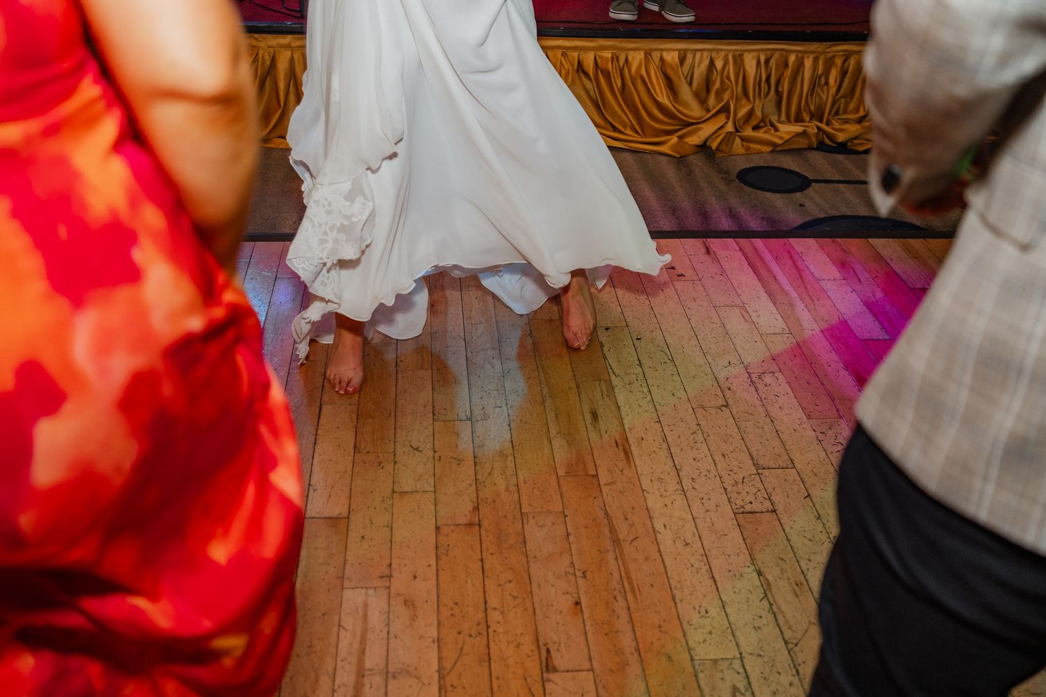 People dancing on a rustic wooden floor illuminated by red and purple party lights during a celebration.