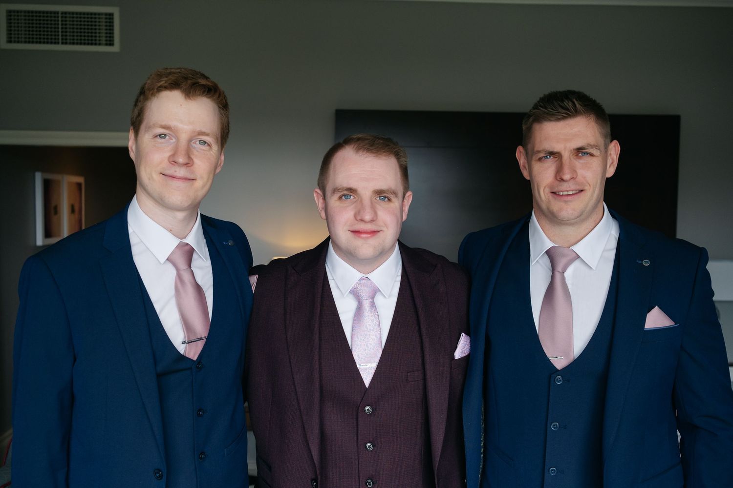 Group of groomsmen in matching suits with burgundy and navy color scheme.
