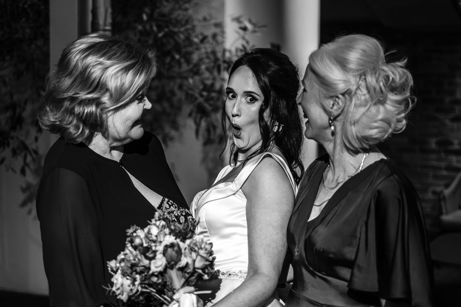 A black and white portrait of three wedding guests sharing a tender moment with flowers.