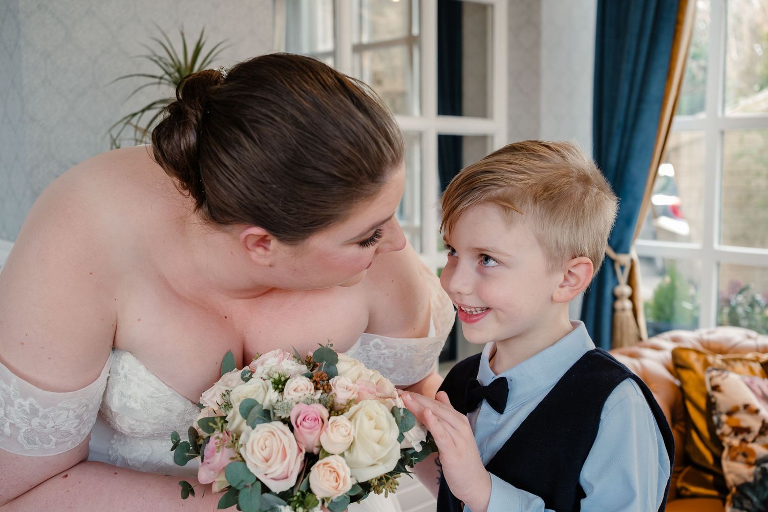 Sweet moment between bride and young ring bearer with pink rose bouquet.